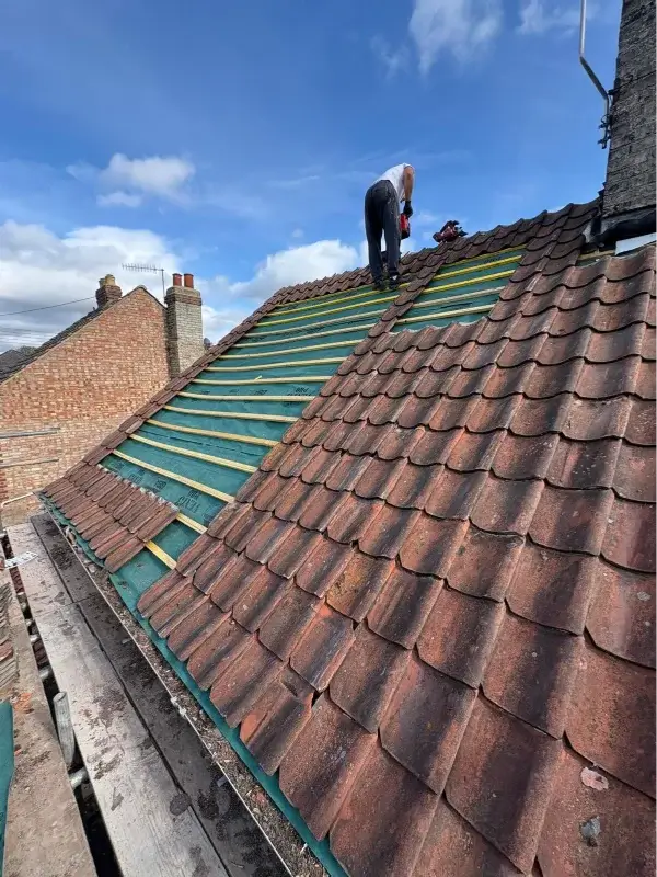 Roofer relaying pantiles over new breathable membrane and timber battens during re-roofing. By Norfolk Exterior Solutions.
